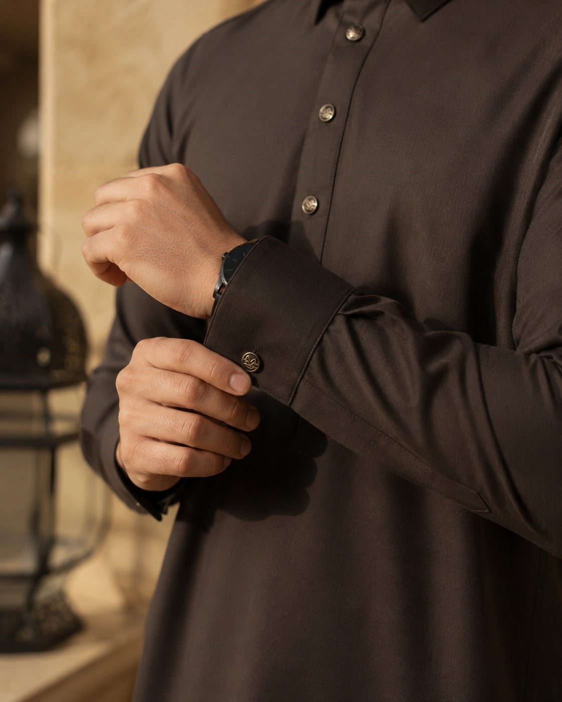 Elite chocolate brown thobe by Al-Emara displayed on a mannequin, showcasing traditional Islamic men's attire with detailed embroidery.